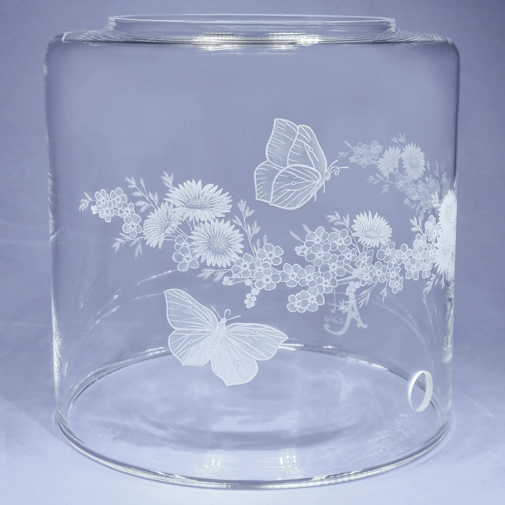 Vorratstank aus Glas für einen Acala Wasserfilter in klarem Glas mit dem gravierten Kranz,umlaufende um das runde Glas.In dem Granz sind Vergissmeinnicht, Schmetterlinge und Gänseblümchen.Linke Ansicht.