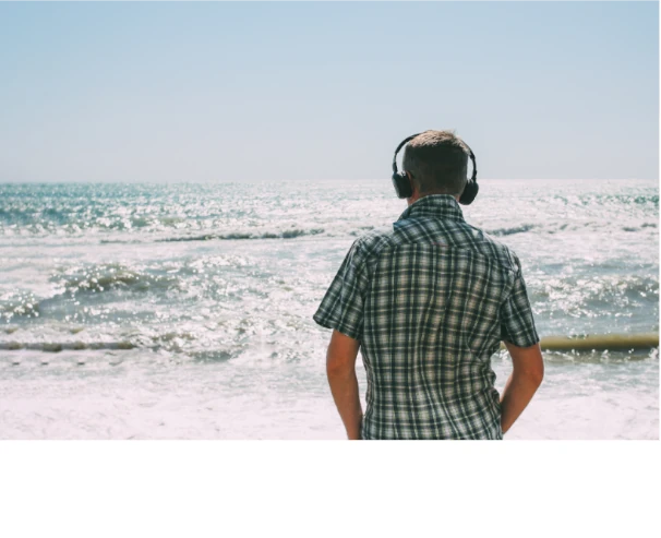 junger mann steht vor dem Meer mit einem Kopfhörer auf dem Kopf und Blickt aufs Mees