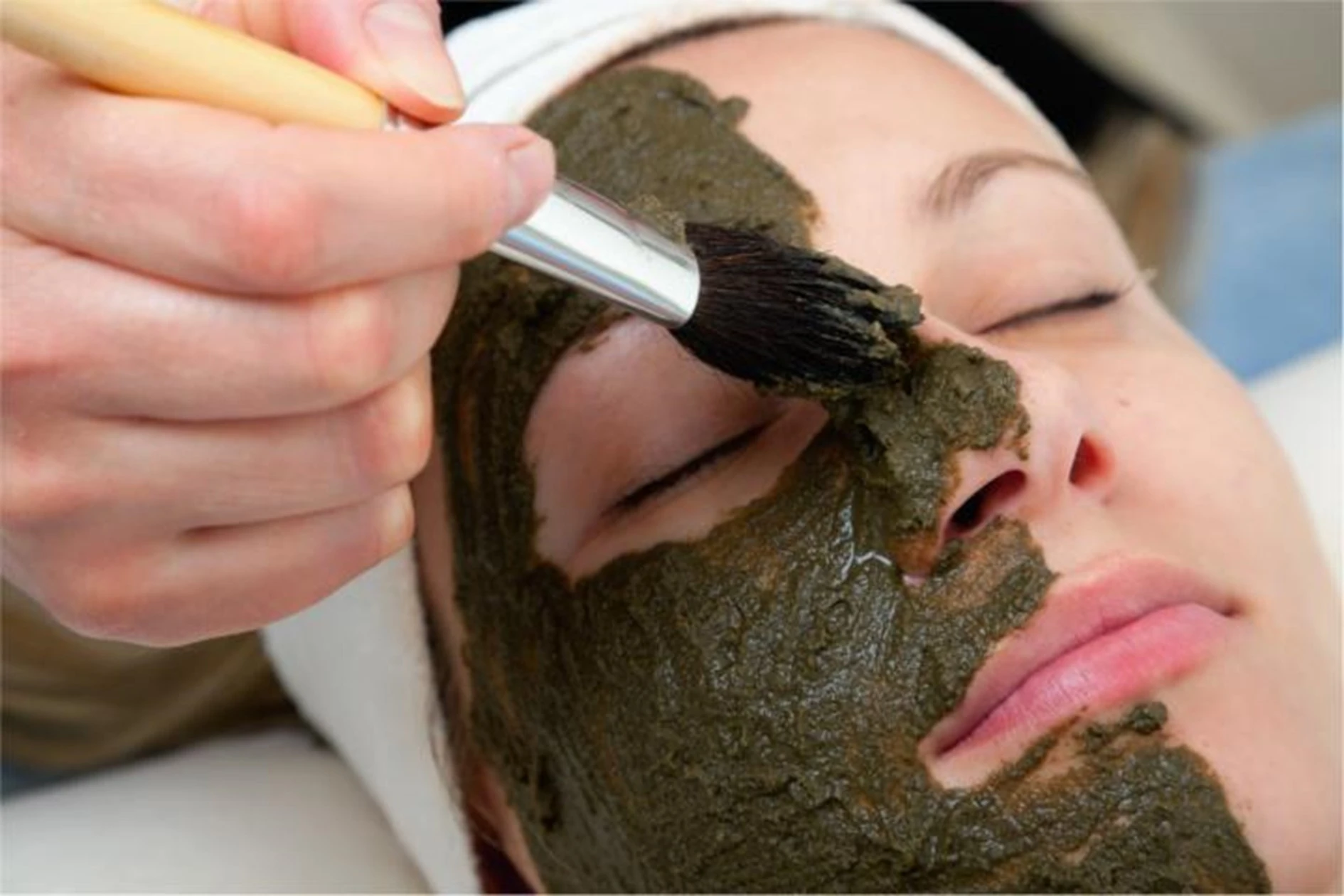 Aktivkohlepaste wird mit Pinsel auf das Gesicht einer Frau aufgetragen. Das Bild ist ein Teil des Acala Blogbeitrages:  Aktivkohle, Anwendung und Hintergründe