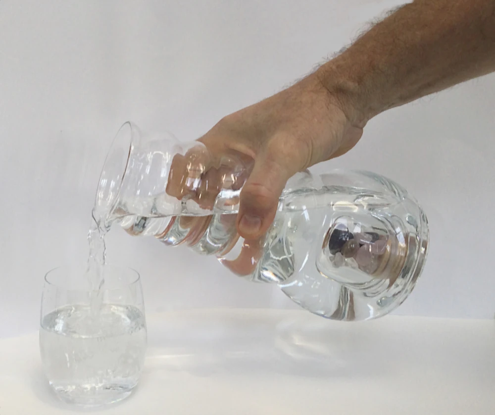 männliche Hand gießt Wasser aus dem Acala Cadus Krug in ein Trinkglas