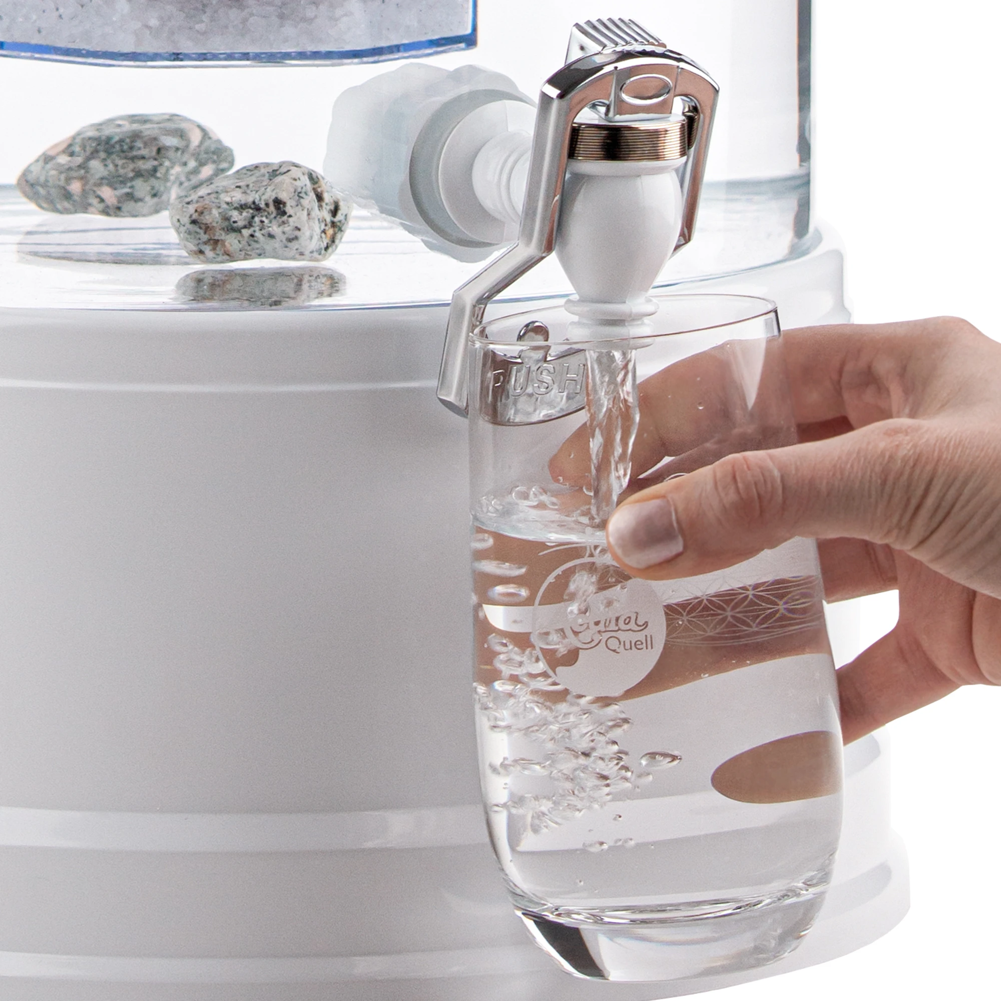 Zu sehen ist der Kunststoff Wasserhahn in weiß für Acala Stand Wasserfilter an einem Glastank in kristallklar montiert. Eine Hand drückt ein Glas gegen den silbernen Bügel, Wasser läuft in das Glas.