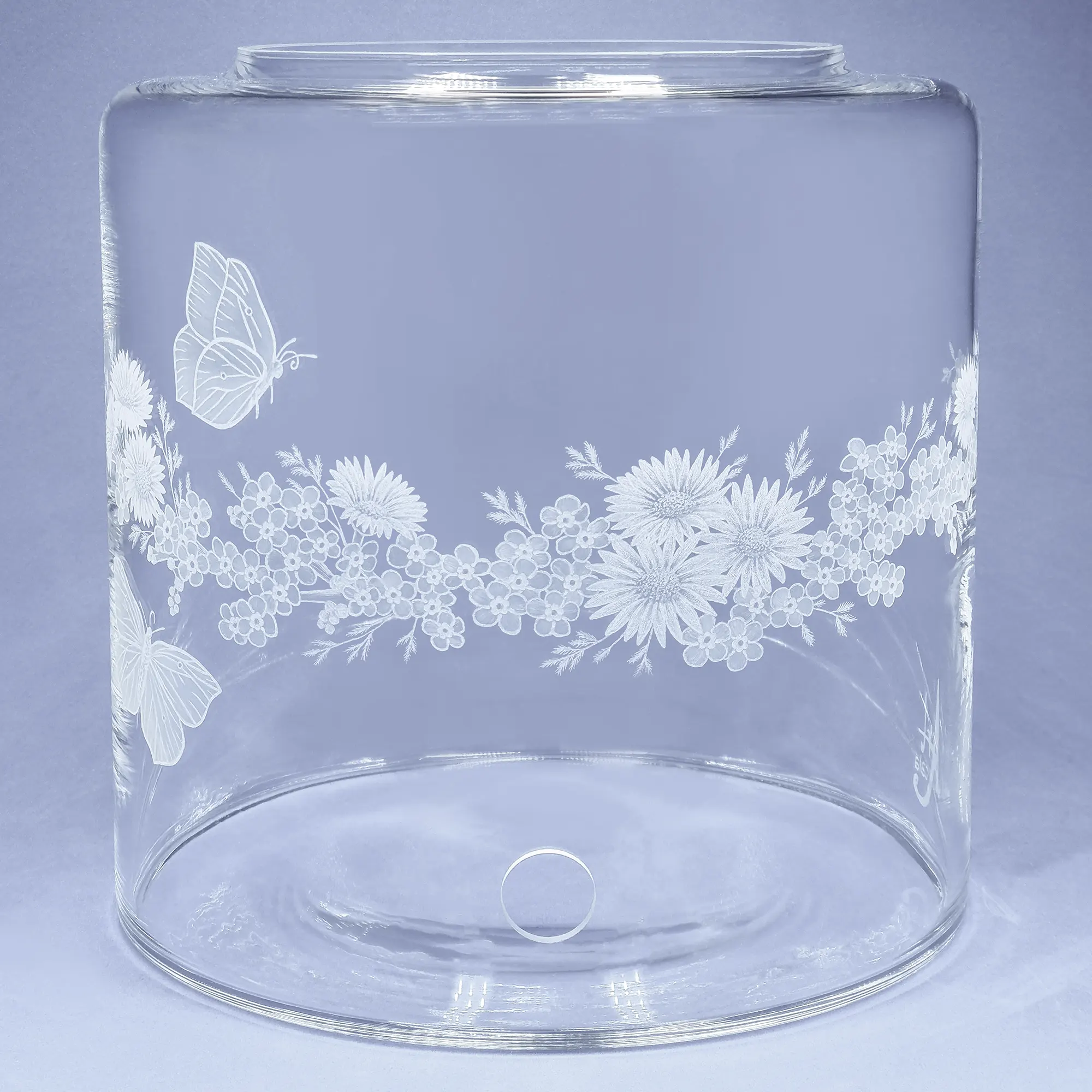 Vorratstank aus Glas für einen Acala Wasserfilter in klarem Glas mit dem gravierten Kranz,umlaufende um das runde Glas.In dem Granz sind Vergissmeinnicht, Schmetterlinge und Gänseblümchen.Vorderansicht.